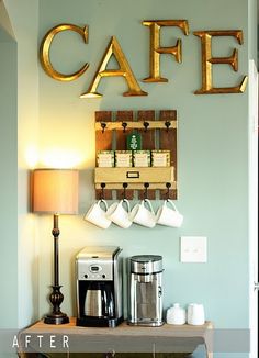 there is a coffee maker and some cups on the counter in this kitchen with gold letters above it