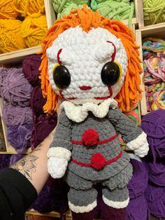 a crocheted doll with orange hair and big eyes sitting in front of colorful yarns