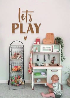 a toddler plays with his toys in the playroom, while it's written let's play on the wall