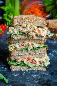 three sandwiches stacked on top of each other with vegetables and herbs in the back ground