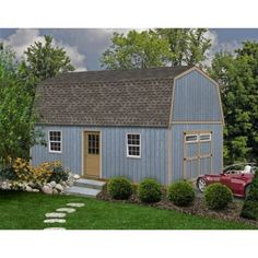 a small blue barn with a red car parked in the yard next to some bushes