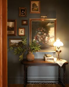 a painting is hanging on the wall next to a table with a lamp and flowers