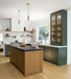 a large kitchen with green cabinets and wooden flooring is pictured in this image, there are two hanging lights above the island