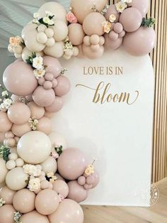 balloons and flowers are arranged in the shape of a heart on a white sign that says love is in bloom