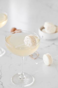 two glasses filled with drinks sitting on top of a white marble table next to shells