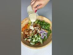 someone pouring dressing onto a salad in a wooden bowl