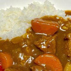 a white plate topped with meat and vegetables covered in gravy next to rice