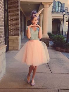 a woman standing on the sidewalk wearing a pink tulle skirt and crop top with her hands to her face