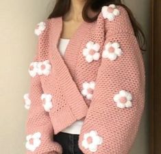 a woman wearing a pink cardigan with white flowers on the sleeves and back, standing in front of a door