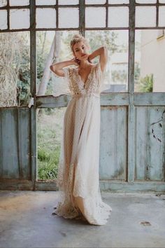 a woman standing in front of an open door wearing a white dress and holding her arms behind her head