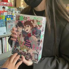 a woman in a black mask is looking at a book with an anime cover on it