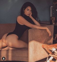 a woman in a black bodysuit sitting on a couch