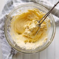 a glass bowl filled with yellow batter on top of a white table next to a gray towel