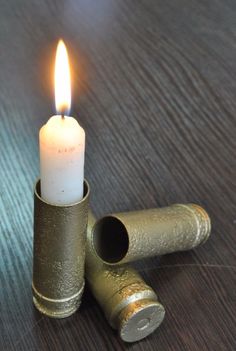 a lit candle is sitting on top of two brass cylinders that are resting on a wooden table