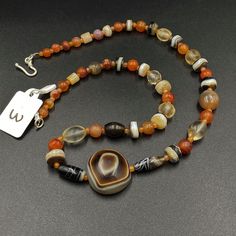 The beautiful mala necklace consist of Himalayan luk Mik or we called them magic eye bead as well in the center of the mala necklace with Banded Agate and carnelian and crystals Luk Mik means (Goat's eyes) in Tibetan Natural found from Himalaya Tibet dating more than 1000 yrs. The origin of this beads from Himalaya Tibet but also can found in India, Nepal and Pakistan too They were used as a special charm Jewelry and amulet at that time period very good condition They were used in prayers mala a Spiritual Amber Beads And Cabochons With Natural Stones, Spiritual Amber Beads With Natural Stones, Bohemian Mala With Natural Agate Stones, Agate Mala With Natural Stones In Round Beads, Bohemian Agate Mala With Natural Stones, Agate Mala With Natural Stones And Round Beads, Bohemian Agate Mala, Unique Carnelian Necklace For Meditation, Spiritual Agate Bead Necklaces