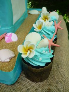 a cupcake with blue frosting and flowers on top is sitting in front of a bag