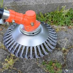 an orange and black brush sitting on top of a metal object in the grass next to some plants