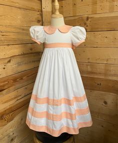 a white and pink dress on a mannequin stand in front of wood planks