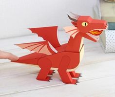 a red paper dragon sitting on top of a wooden table next to a planter