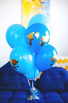 blue balloons with gold confetti on them are sitting on a blue ottoman in a bedroom