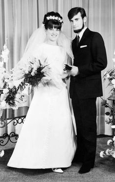 a man and woman standing next to each other in front of a table with flowers