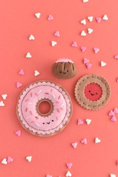 two doughnuts with sprinkles and hearts on a pink background next to each other