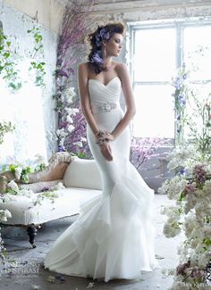 a woman in a white wedding dress standing next to a couch with flowers on it