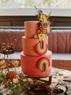 a multi - tiered cake with flowers on top sits on a table in front of a window