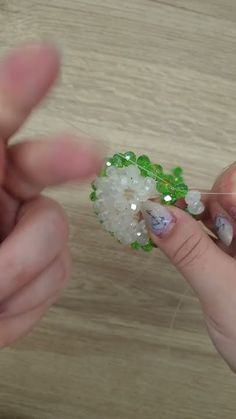 two hands are working together to make a beaded flower with white and green beads