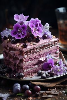 a piece of cake with purple flowers and berries on it sitting on a plate next to a glass of tea