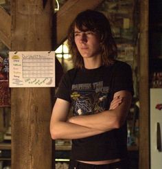 a young man standing with his arms crossed in front of a wooden wall and sign