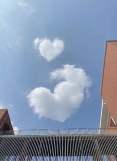 there is a heart shaped cloud in the blue sky above some buildings and a fence