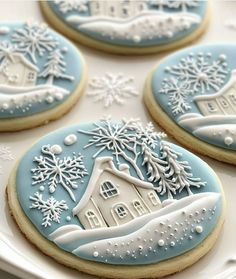 four decorated cookies on a white plate with snowflakes and houses in the background