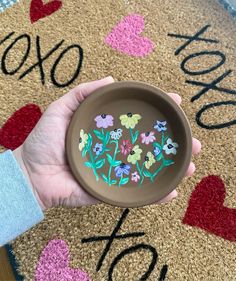 a person holding a bowl with flowers painted on it in front of a welcome mat