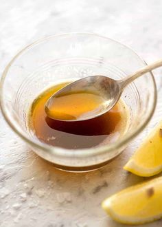 a glass bowl filled with liquid next to sliced lemons and a spoon on a table