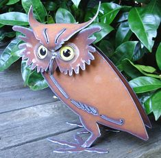 an owl statue sitting on top of a wooden table next to green plants and leaves