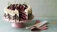 a cake with cherries on it sitting on top of a pink plate next to a knife and fork