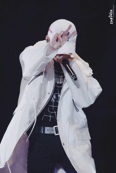 a male in a white jacket and black pants is holding his hands up to his face