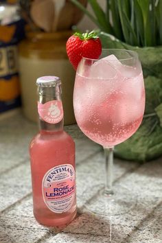 a bottle of rose lemonade next to a glass with a strawberry on top