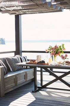 a table and chairs on a deck with flowers in vases next to the water