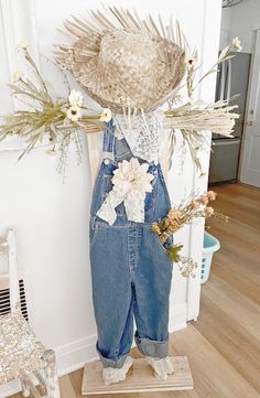 a scarecrow wearing overalls and a straw hat with flowers on his head is standing in front of a door