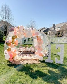 an outdoor birthday party with balloons, cake and letters on the grass in front of a fence