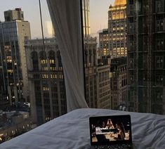 an open laptop computer sitting on top of a bed in front of a cityscape