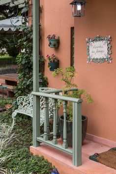 a green bench sitting on the side of a pink building next to flowers and plants