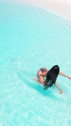 a woman is floating in the water on a surfboard with her long black hair