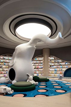 a large white elephant statue sitting on top of a blue rug in a library filled with books