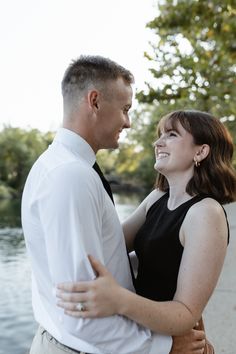 a man and woman standing next to each other in front of a body of water