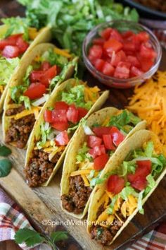 three tacos on a cutting board with cheese, tomatoes and lettuce