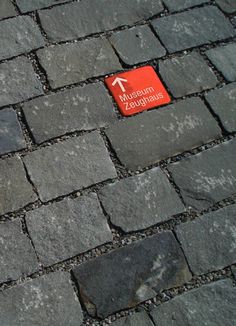 a red sign is on the cobblestone pavement with an arrow pointing in opposite directions