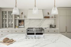 a large kitchen with marble counter tops and white cabinets, along with hanging lights above the stove